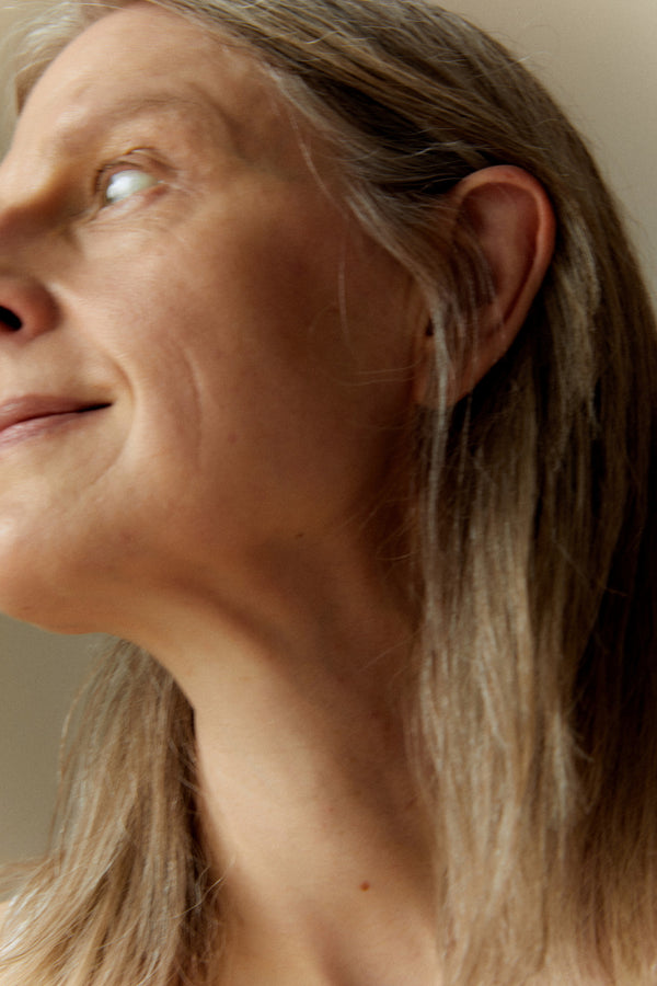 Close-up side profile of a woman with long light brown hair, looking upward, against a soft beige background.